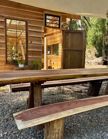 A long wooden table and benches under a shade sail beside a timber building