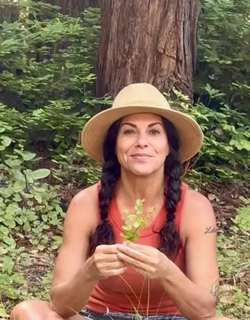 A woman in a straw hat sitting cross-legged in the forest
